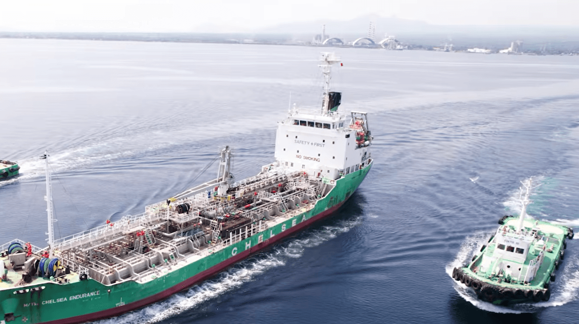 An aerial view of a Chelsea Logistics tanker moving through the water, escorted by a tugboat.
