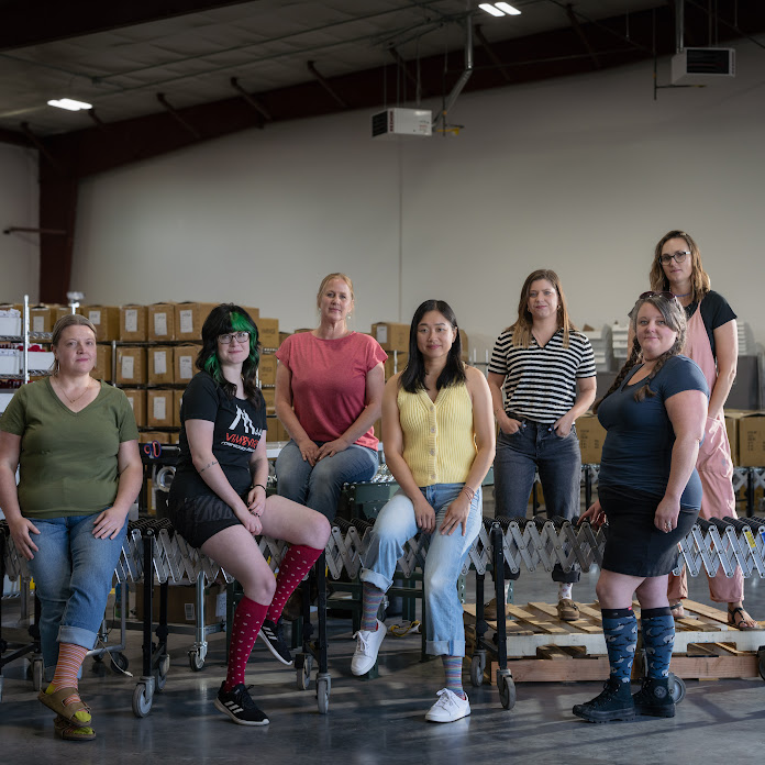 The Vim & Vigr team stand together in their warehouse with a conveyor belt behind them. 