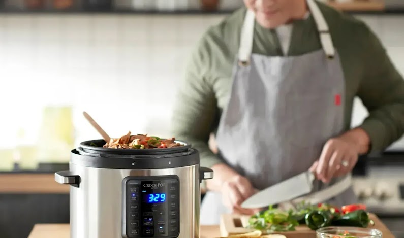 A chef wearing an apron cooking in the kitchen, using a smart slow cooker device in the foreground.