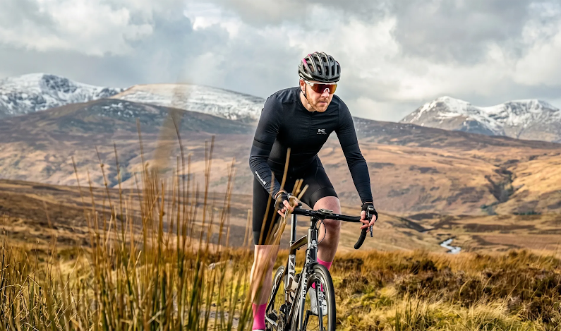 A man riding a bike along a mountain range, with sunglasses and helmet on.