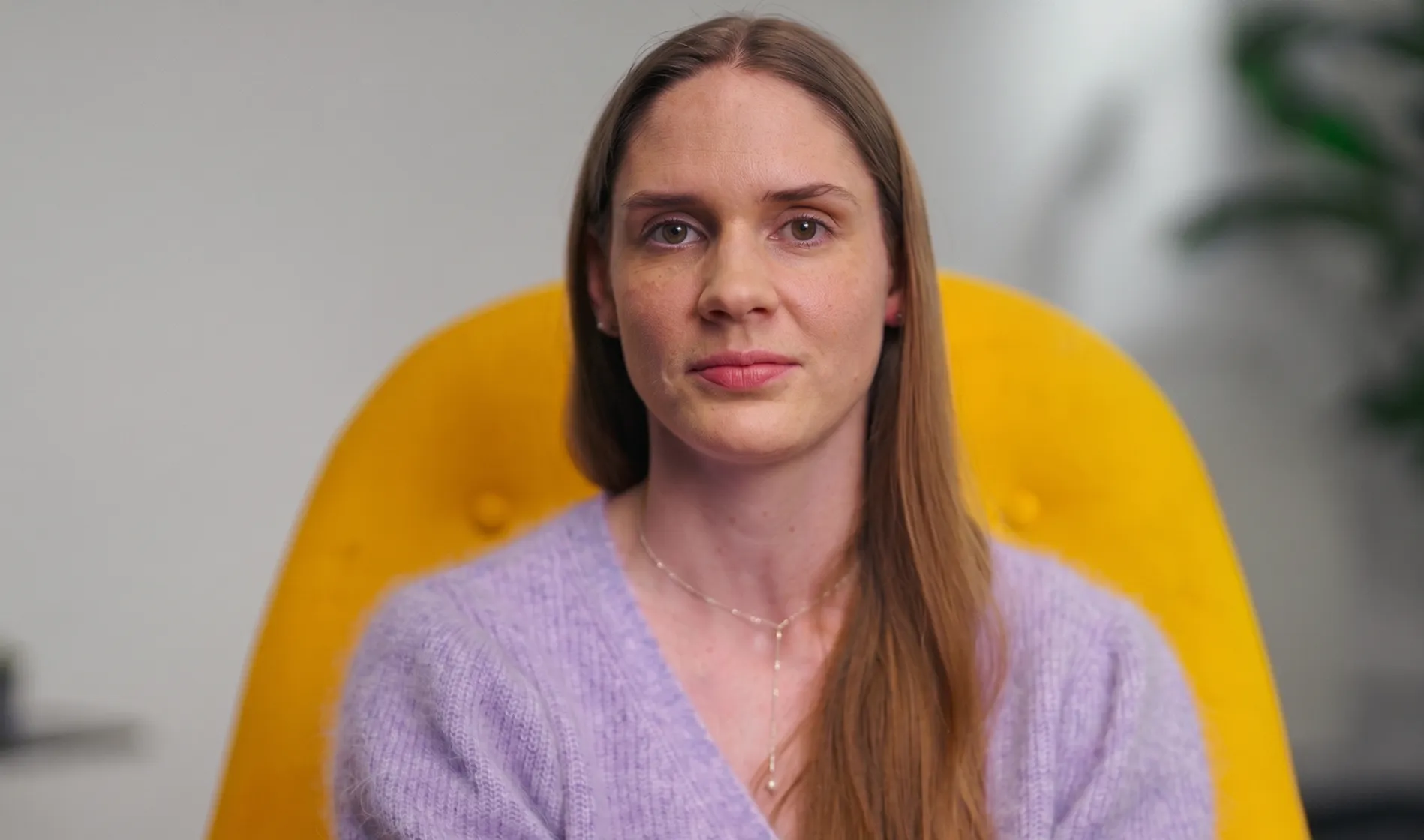 A woman sits facing the camera in a yellow chair.